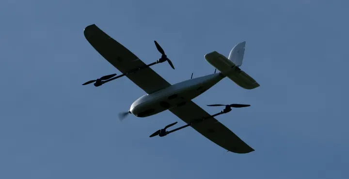 VTOL fixed-wing drone in flight against a blue sky